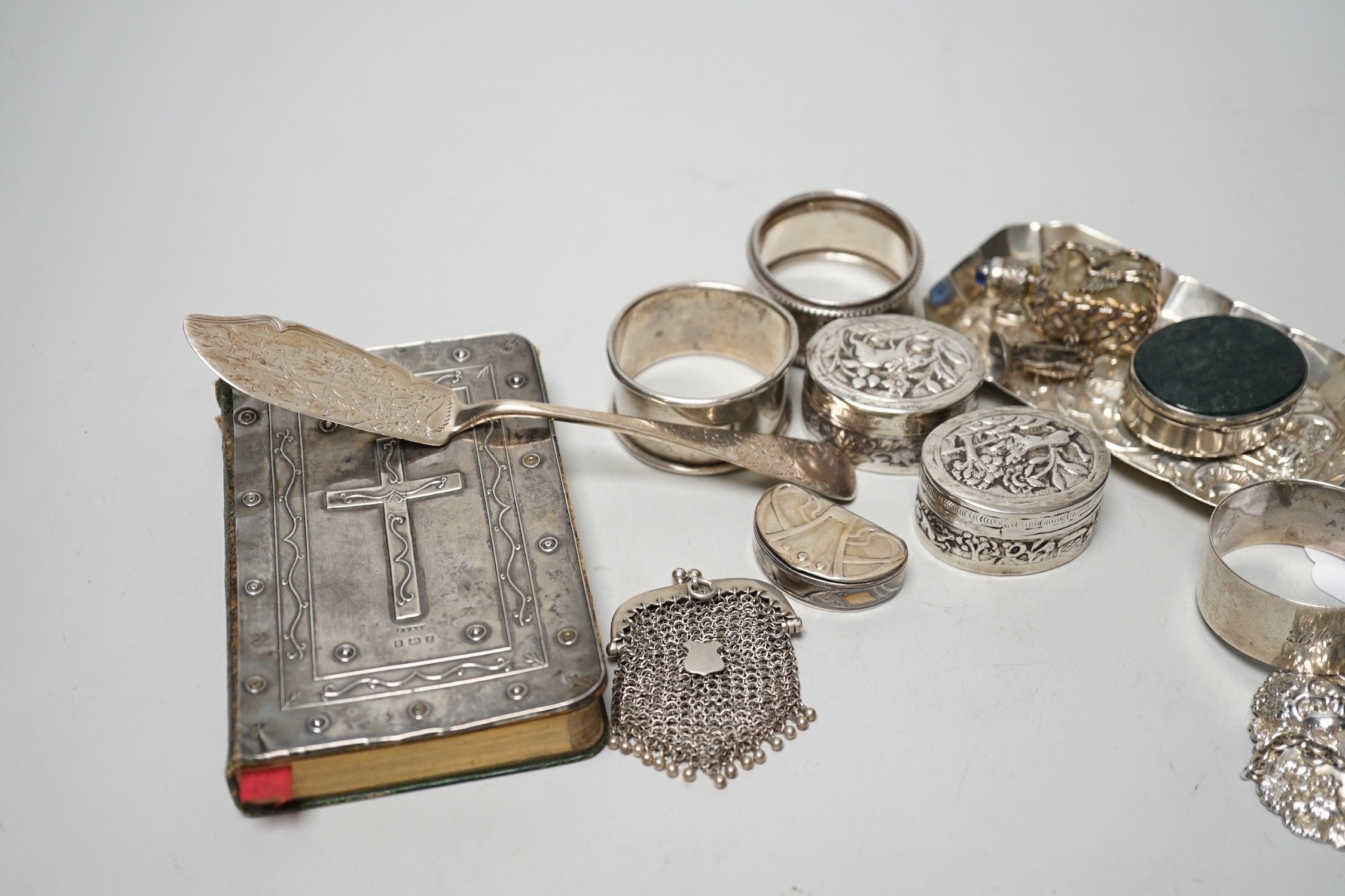 Sundry small silver including four assorted napkin rings, mounted bible, butter knife, pin tray, wine label etc. together with two white metal oval pill boxes, a moss agate mounted oval pill box and scent bottle.